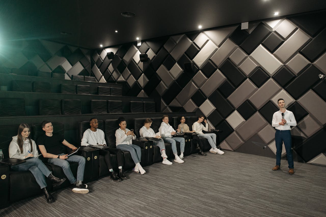 Speaker addressing a diverse audience in a modern theater setting.